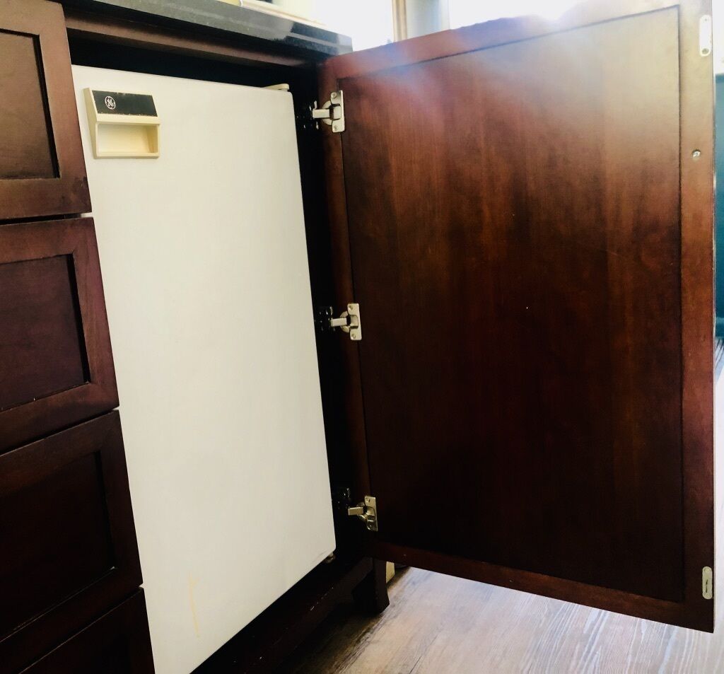 Un meuble en bois abritant un appareil électroménager blanc, peut-être un réfrigérateur, et une porte dotée d’un loquet métallique.
