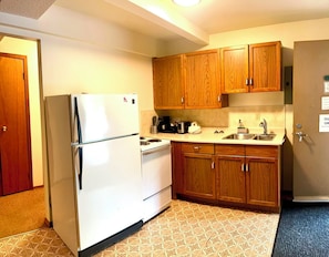 Una cocina compacta con armarios de madera, un refrigerador blanco, una estufa y un lavabo.
