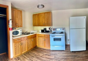 A kitchen with wooden cabinets, a microwave, stove, and a refrigerator. - The Voy (Schreiber)