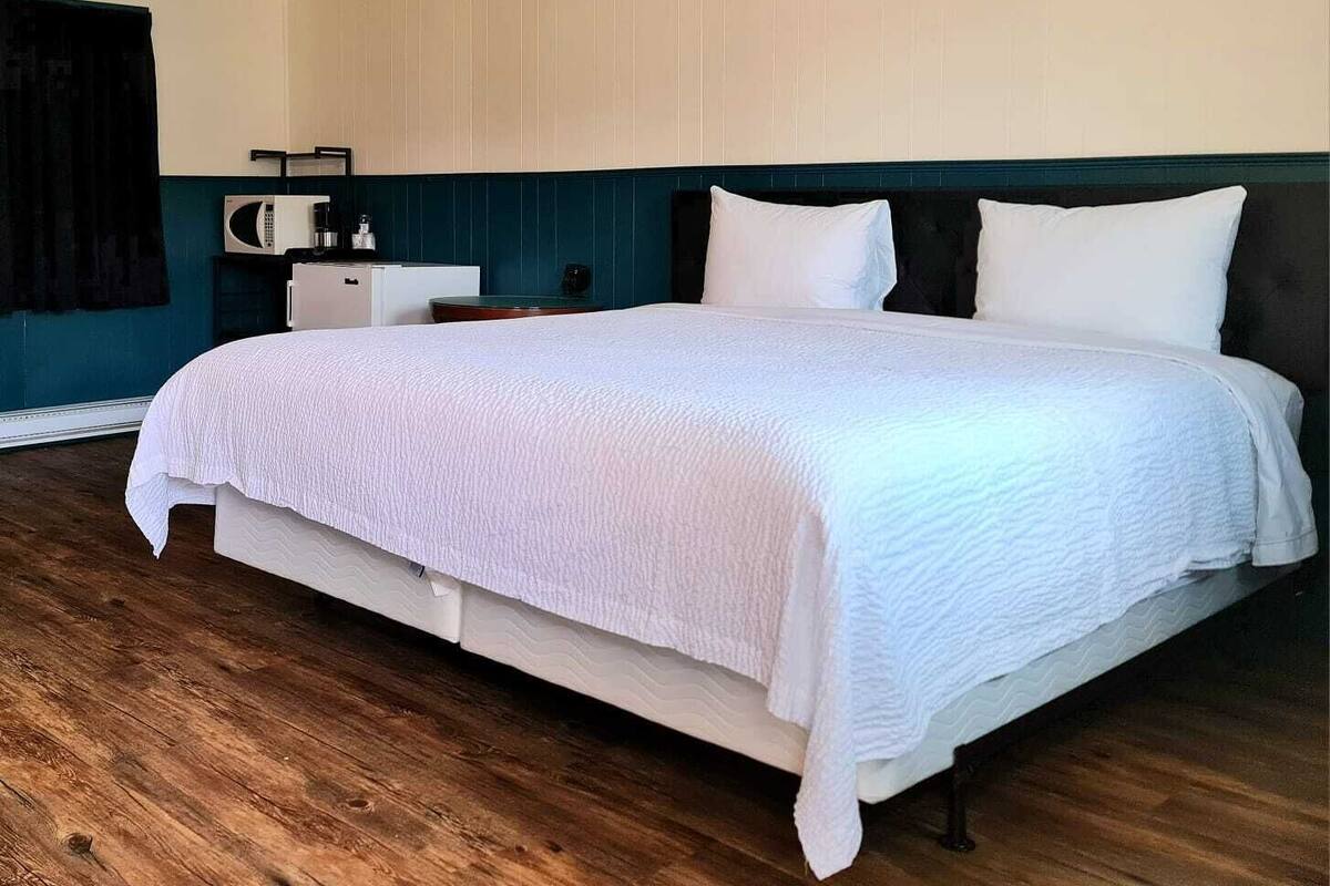 Cama bem arrumada com roupa de cama branca em quarto com piso de madeira e paredes verde-água.