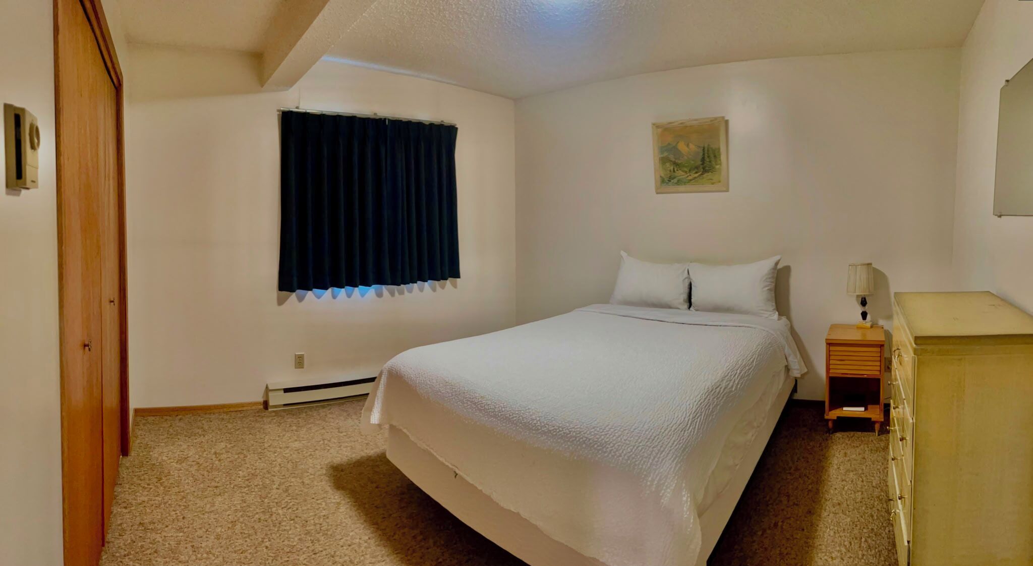 A bedroom with a bed, a nightstand, a dresser, a window with curtains, a wall-mounted picture, and a ceiling vent.