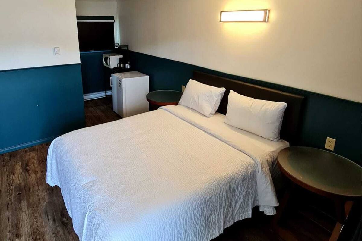 Quarto de hotel com uma cama grande, uma mesinha redonda, micro-ondas e uma cozinha compacta ao fundo.