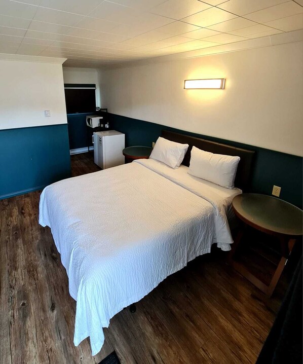 A hotel room with a large bed, a small round table, a microwave, and a kitchenette in the background.