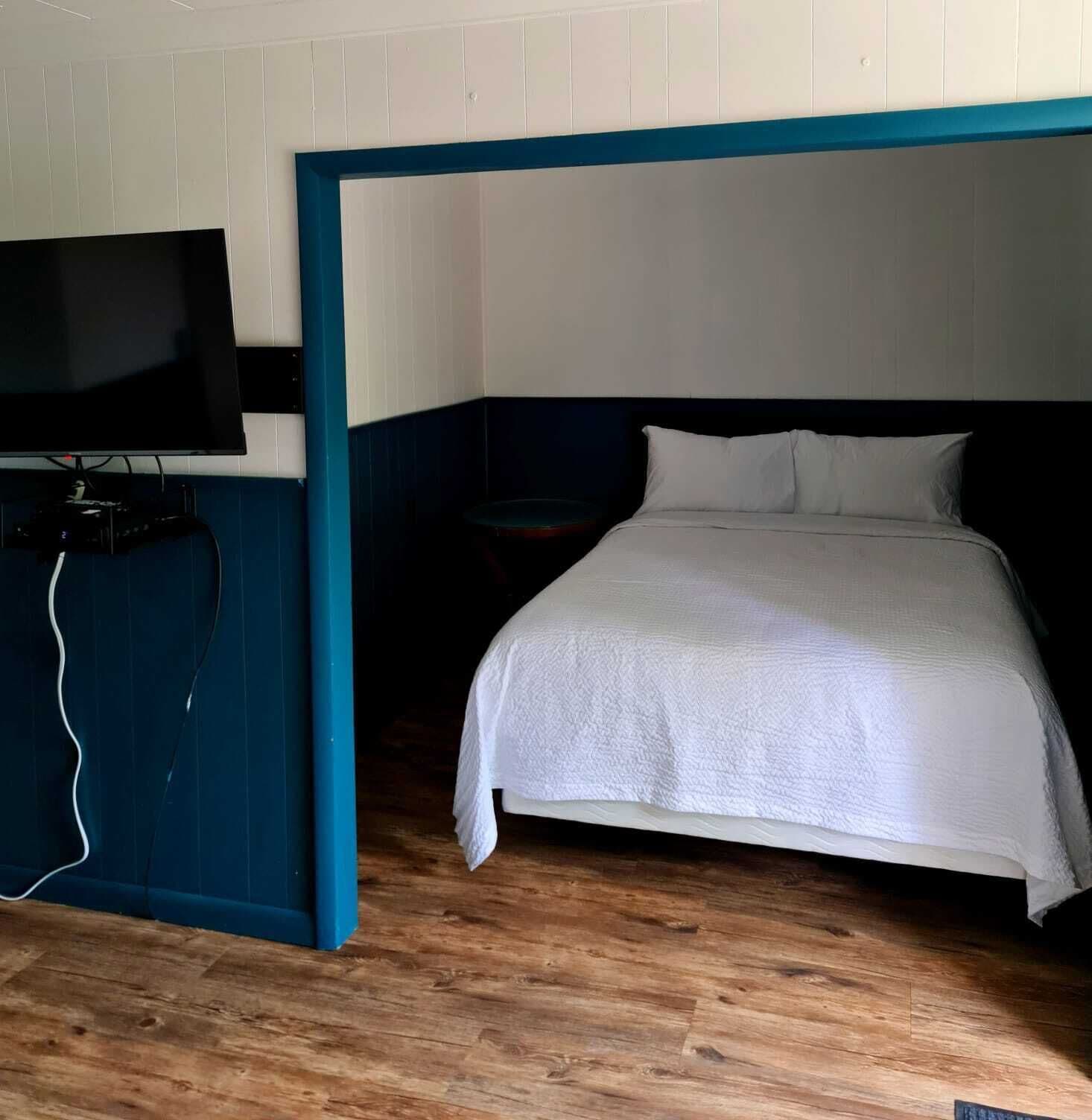 A bedroom with a bed, a TV, and a wooden floor.