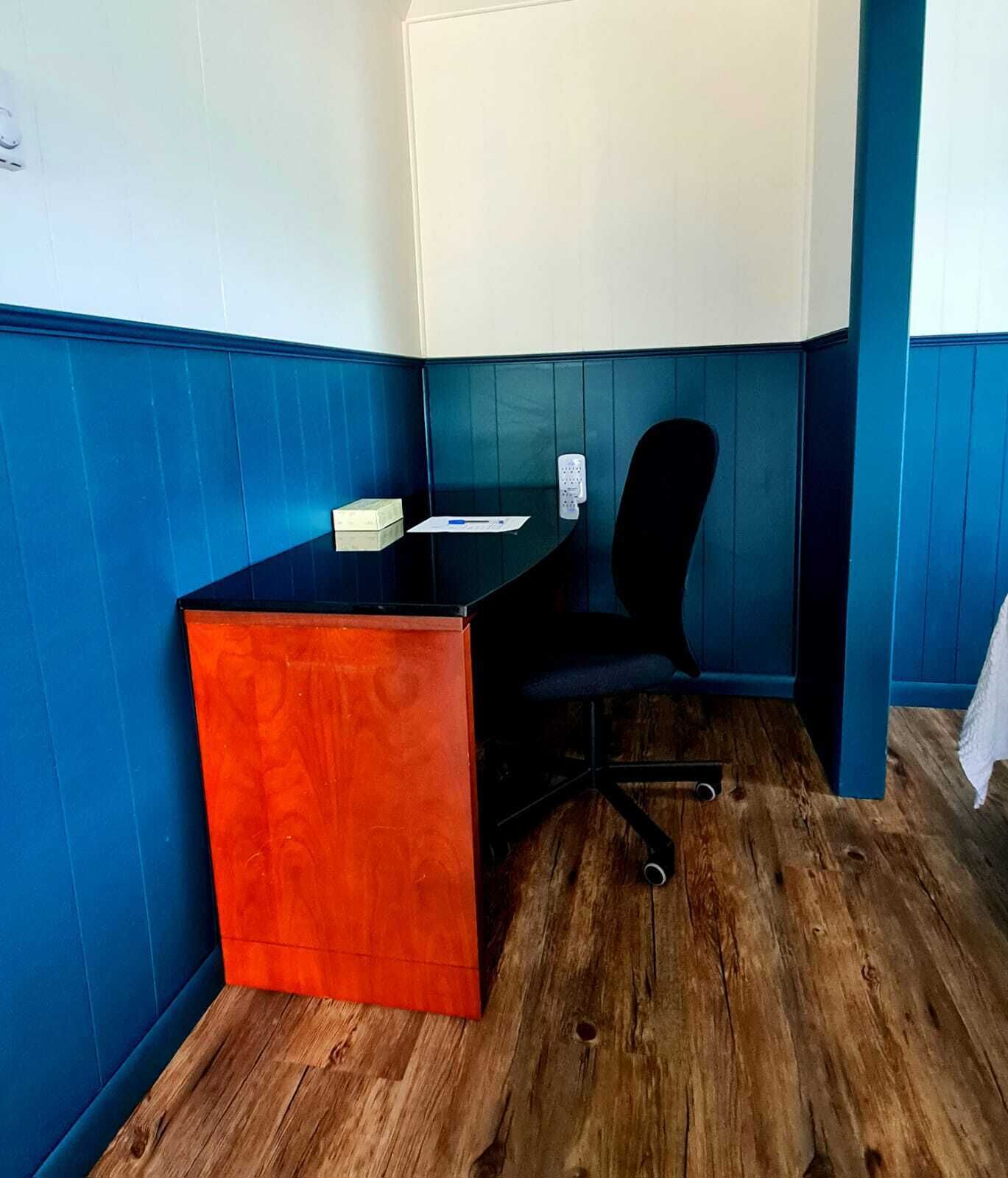 A small office space with a wooden desk, a black office chair, and a white wall-mounted telephone.