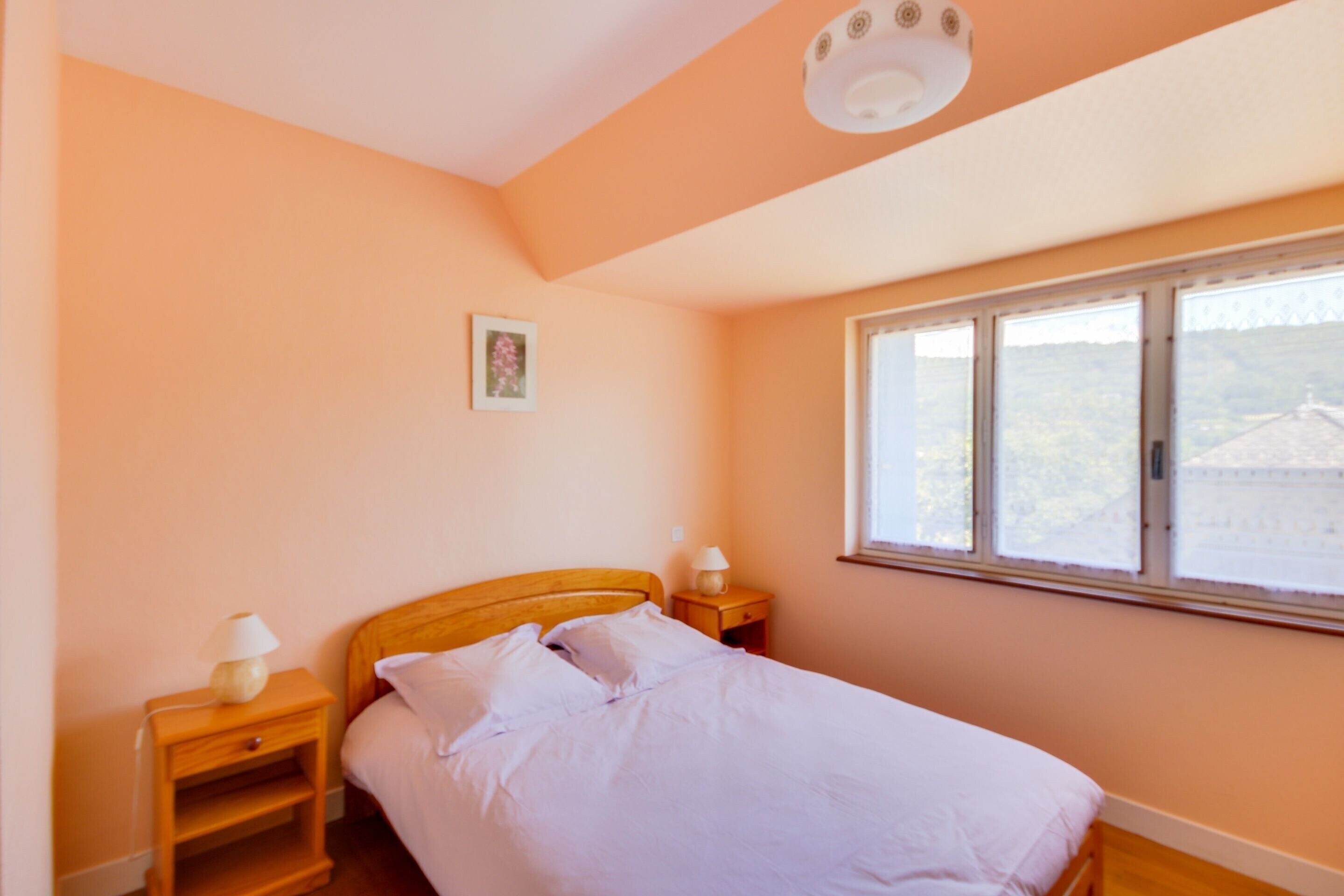 A bedroom with a single bed, a nightstand with a lamp, a window with a view, and a ceiling light fixture.