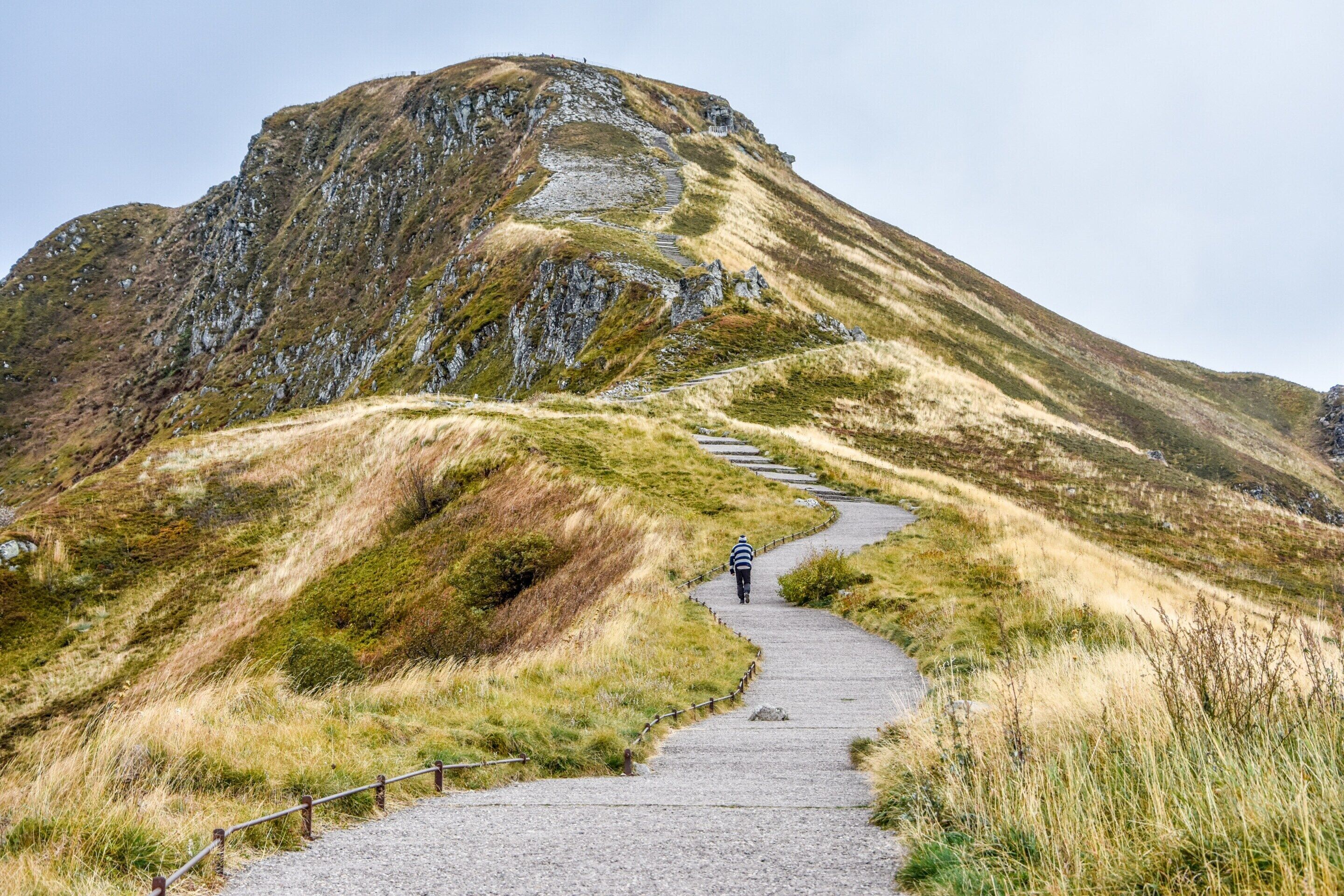 A person walking on a gravel path with a mountain in the background.