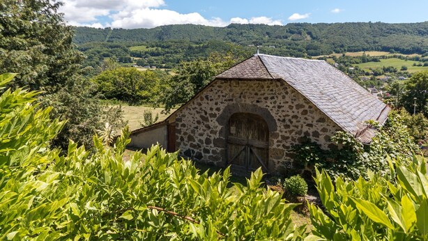 A stone building with a sloped roof, surrounded by lush greenery and hills in the background. - Vic-sur-cere Family Nest (Vic-sur-Cere)