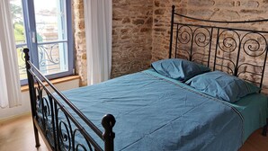 Un letto con struttura in metallo e biancheria azzurra in una stanza dalle pareti in pietra e una finestra con tende.