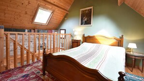 Ein Schlafzimmer mit einem hölzernen Bett, einem Oberlicht, einem Gemälde an der Wand und einem Bücherregal.