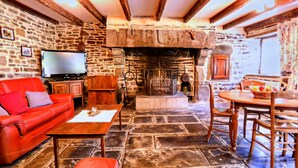 A stone-floored room with a fireplace, a red sofa, a wooden table, and a television. - Alluring Holiday Home With Fenced Garden, Barbecue (Montaigu-les-Bois)