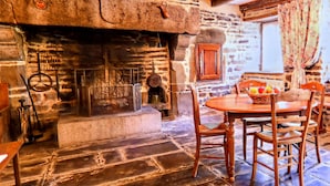 A stone fireplace with a wooden mantel, a stone floor, and a round wooden table with chairs. - Alluring Holiday Home With Fenced Garden, Barbecue (Montaigu-les-Bois)