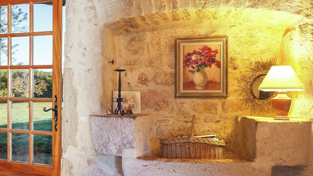 A rustic stone wall with a framed painting, a candle holder, and a lamp. - Forest Hideaway in Saint-caprais (Saint-Caprais)