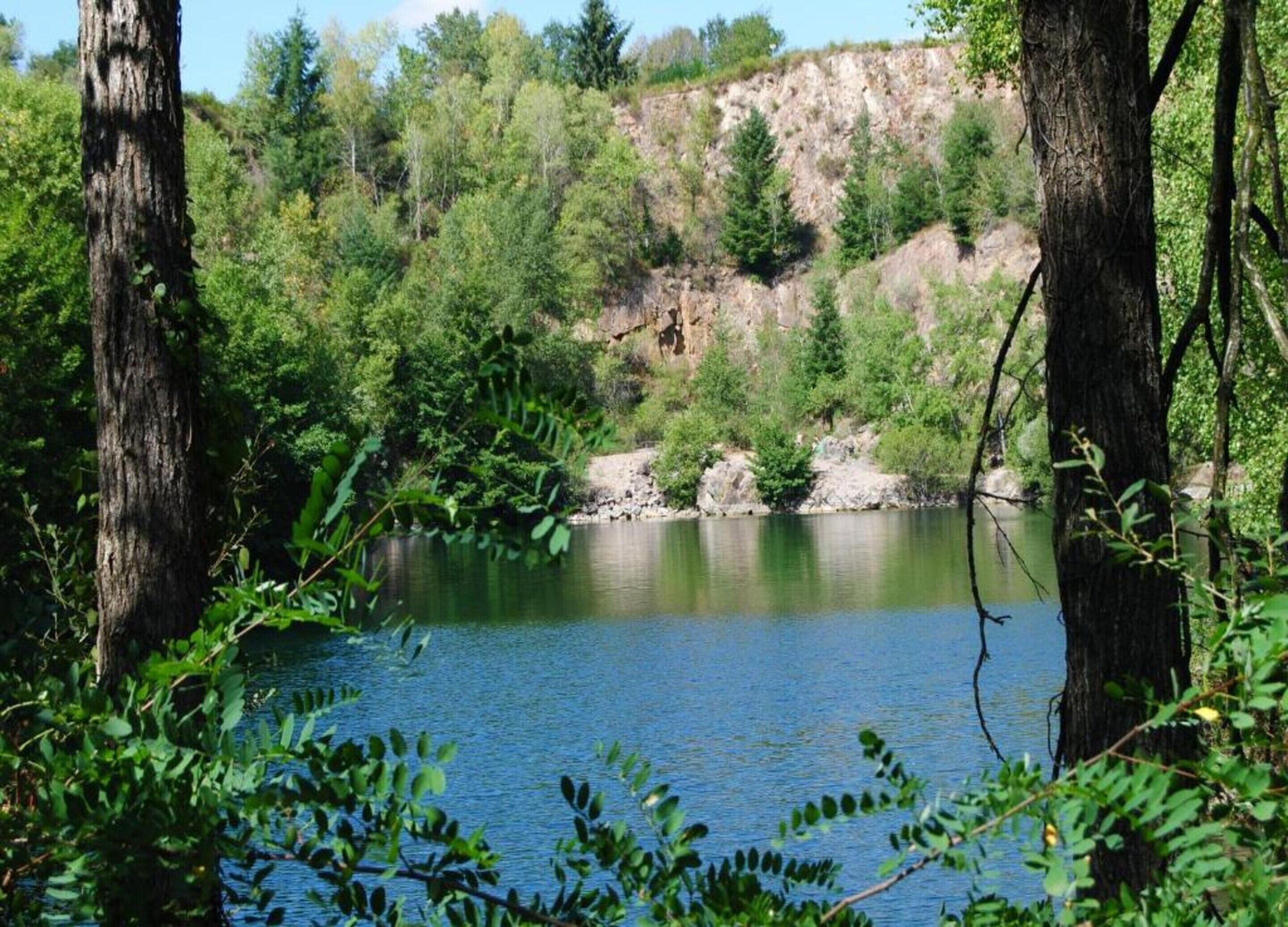 A natural landscape with a calm lake, surrounded by dense greenery and rocky cliffs.