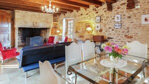 A rustic room with a stone wall, a fireplace, a sofa, and a dining table with chairs. - Forest Hideaway in Saint-caprais (Saint-Caprais)
