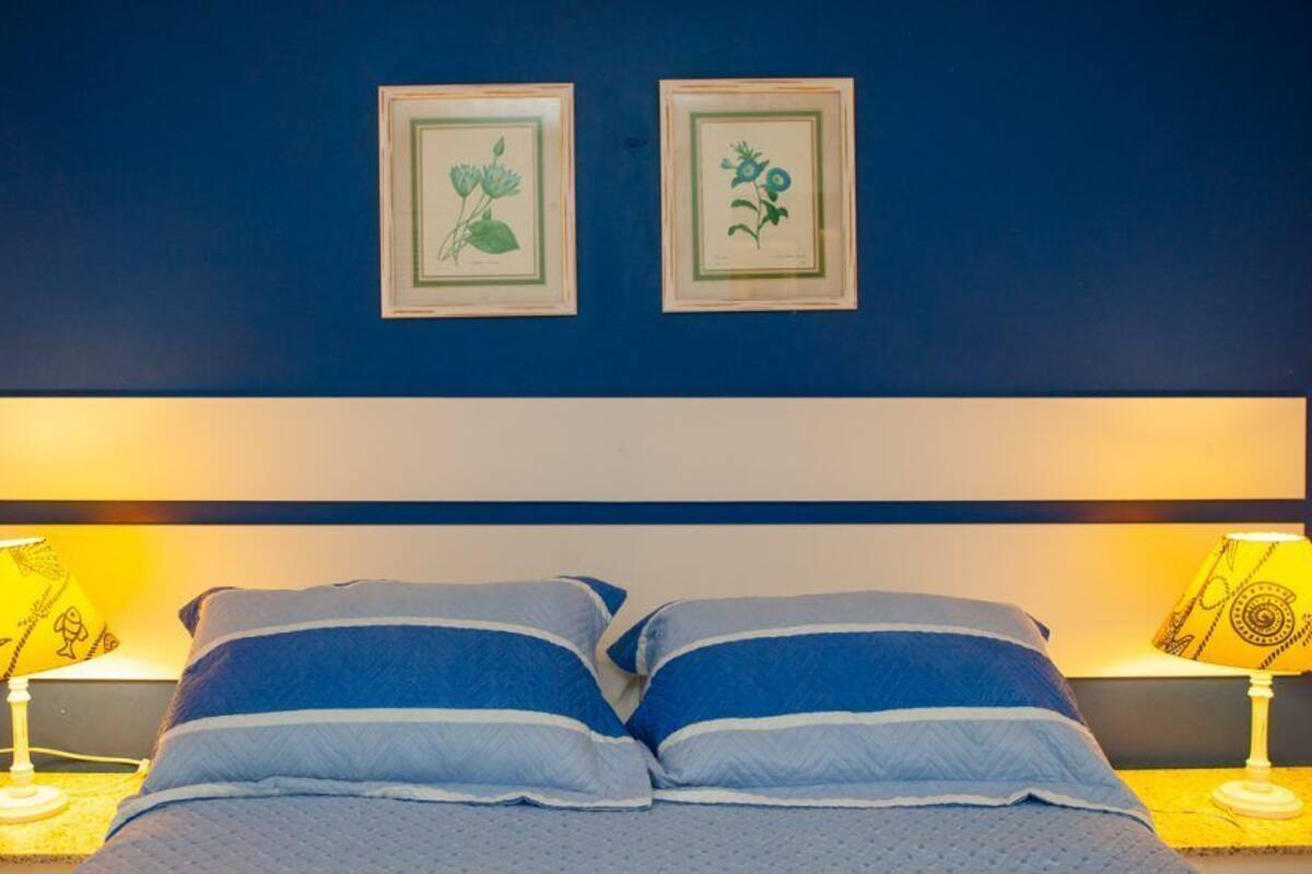 Un dormitorio con una cama, dos lámparas de noche e impresiones botánicas enmarcadas en la pared.