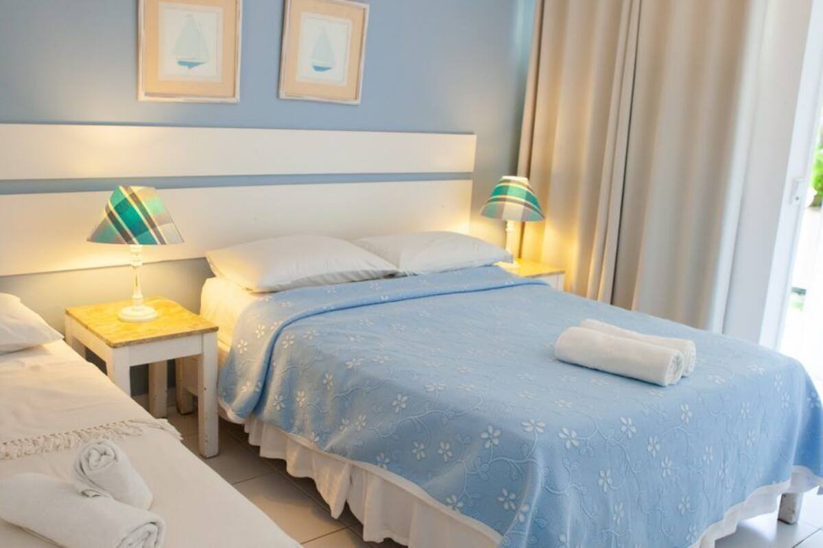 Habitación de hotel con dos camas, un ventanal con cortinas y vistas a zonas verdes.