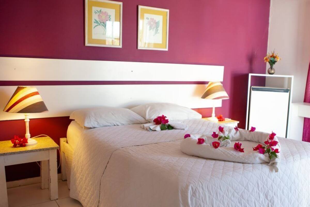 Una habitación de hotel con una cama, dos lámparas de noche, una mesita de noche y un ventanal con cortinas.
