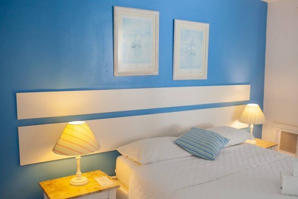 Habitación de hotel con una cama, dos lámparas de noche, un cabecero y dos cuadros en la pared.