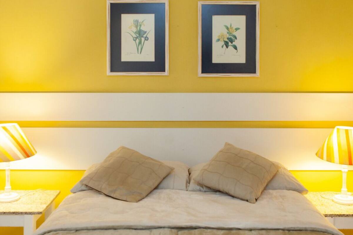 Una cama con dos almohadas, cabecera blanca y dos lámparas de noche.