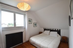 Ein Schlafzimmer mit Bett, Heizkörper, Fenster und einer Pendelleuchte.