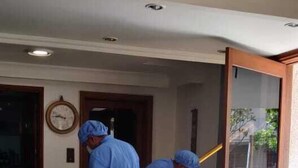 Dos personas con trajes de protección azules limpiando una habitación con un trapeador y un cubo.