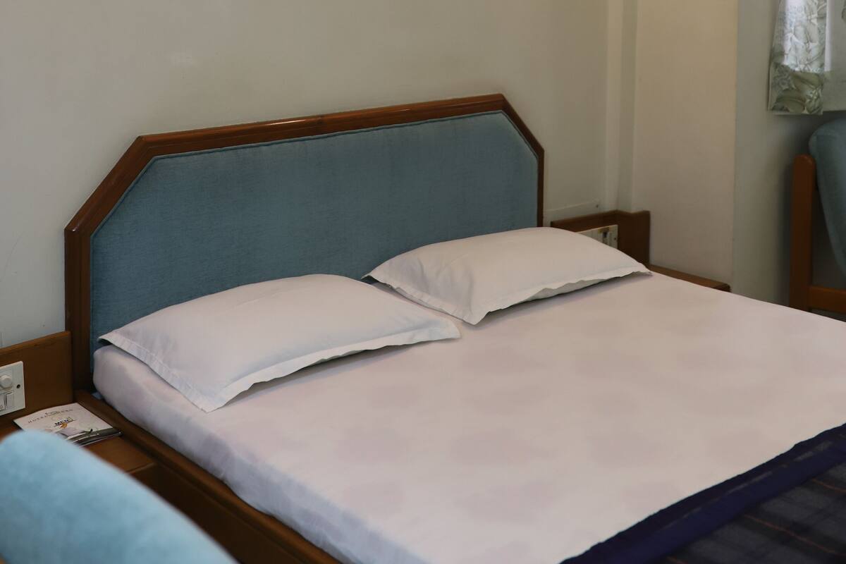 A hotel room with a single bed, a nightstand, a wall-mounted light, and a window with a curtain.