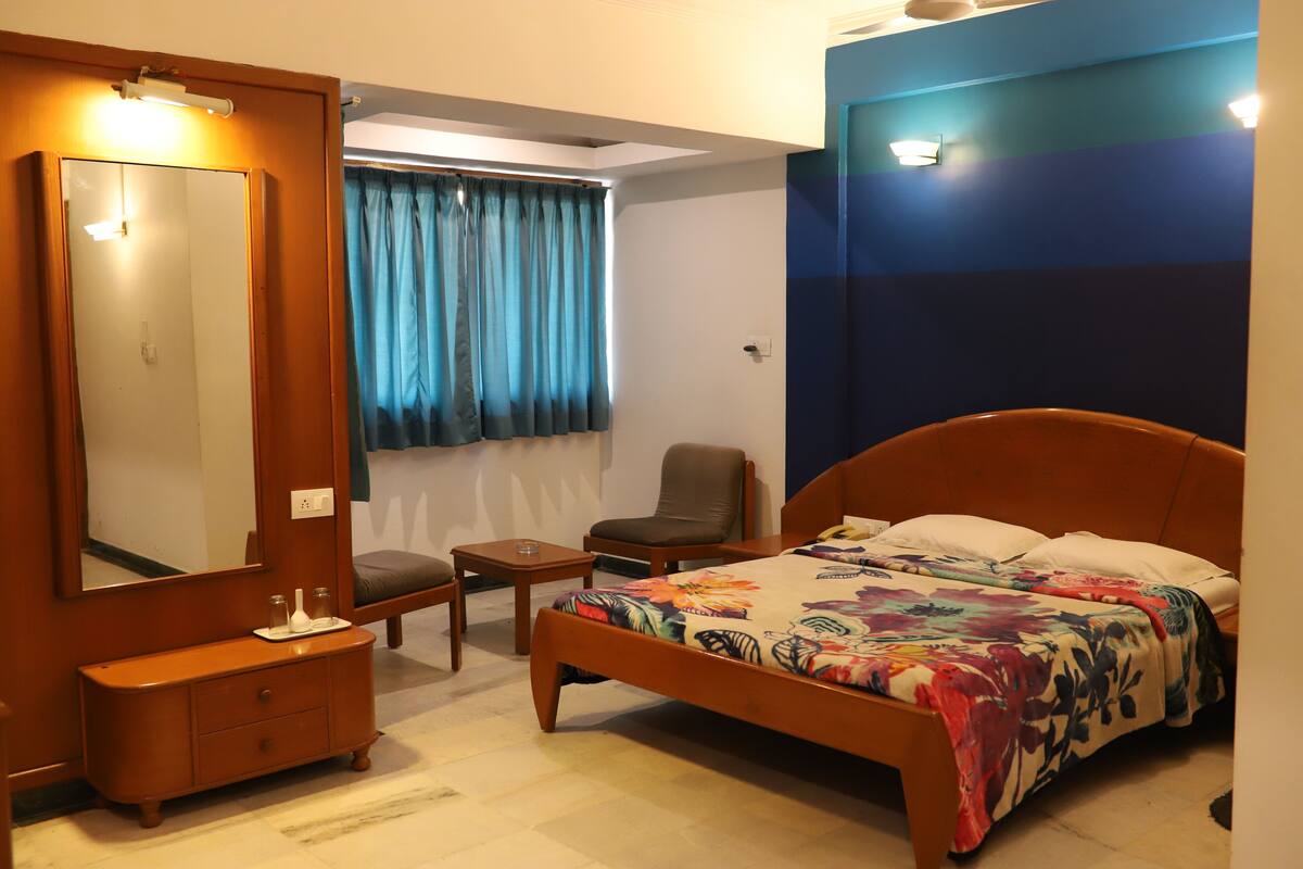 A bedroom with a wooden bed, a nightstand, a chair, a dresser, a mirror, and a window with curtains.