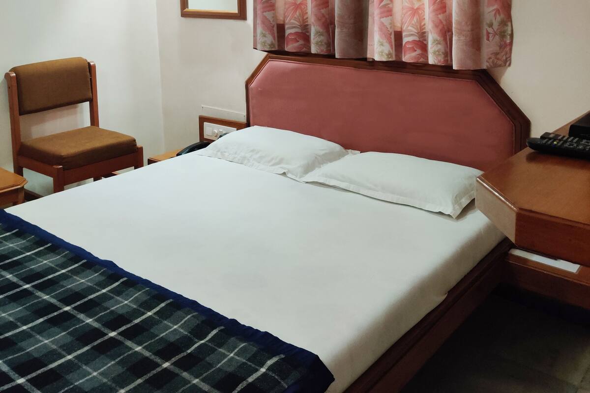 A hotel room with a bed, a chair, a desk, a mirror, and a ceiling fan.