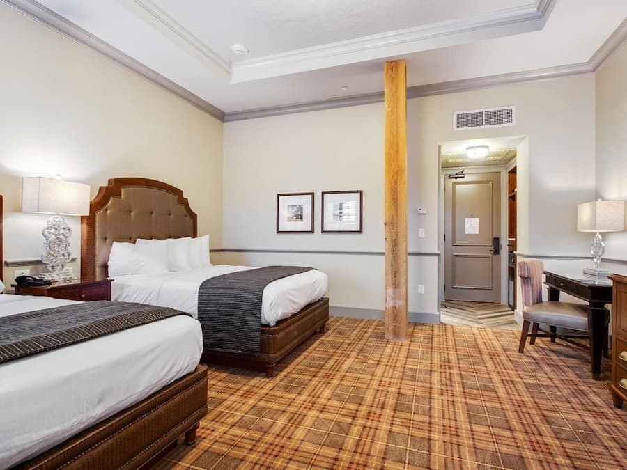 A hotel room with two beds, a desk, a chair, and a wardrobe.