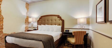 A hotel room with a large bed, a desk, a chair, and a lamp.