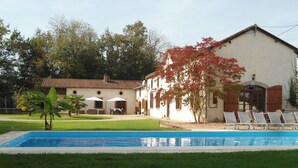 A swimming pool with lounge chairs, a building with a tiled roof, and a tree with red leaves. - Luxurious Holiday Home With Private Pool (Buzon)