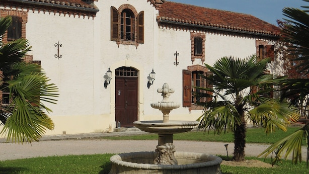 A building with a white facade, a brown door, and a fountain in the foreground. - Luxurious Holiday Home With Private Pool (Buzon)