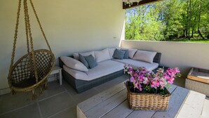A wicker sofa with cushions, a hanging chair, a wicker table with flowers, and a view of trees through a window. - Luxurious Holiday Home With Private Pool (Buzon)