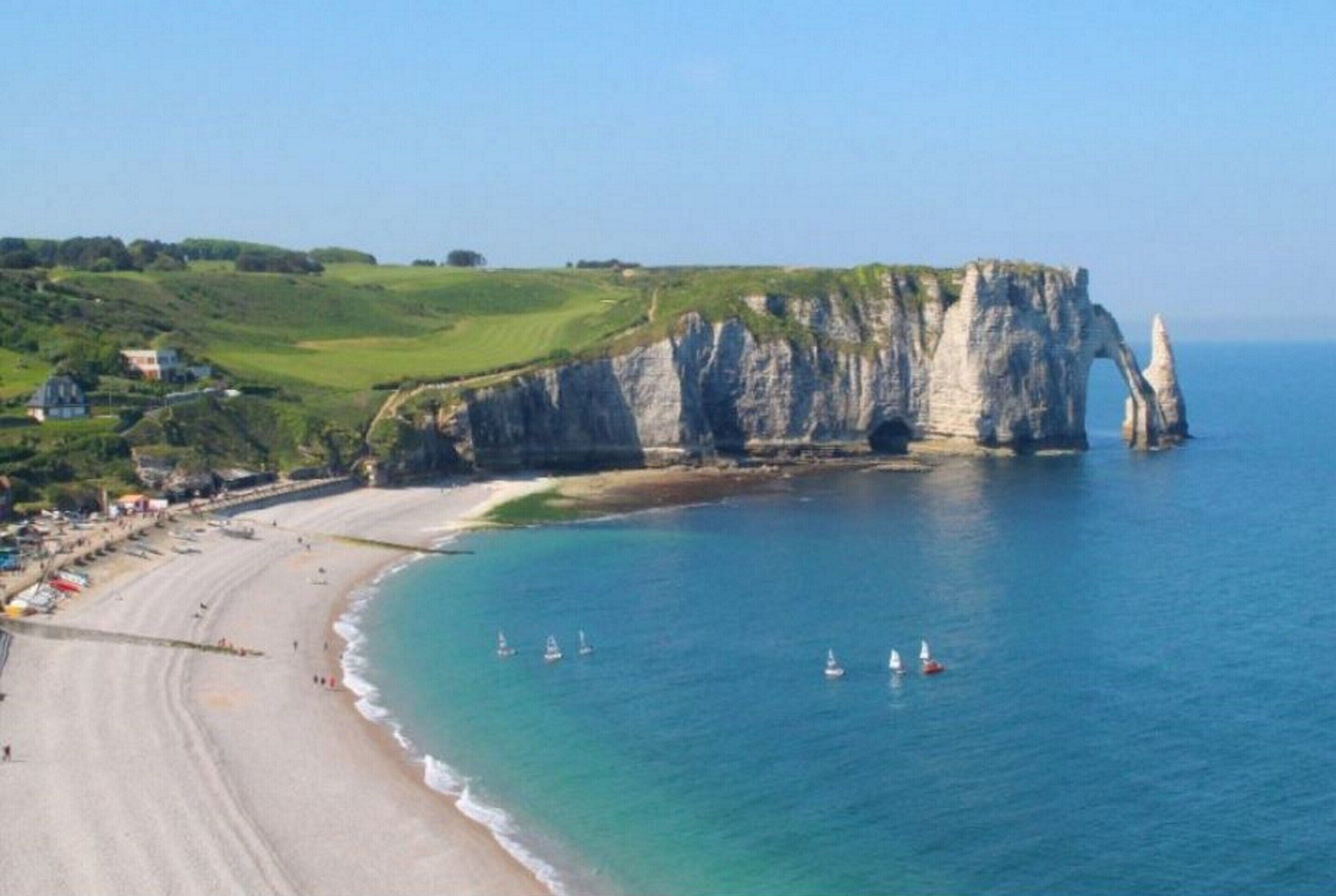 A coastal landscape with cliffs, a beach, and sailboats.