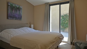 A bedroom with a large bed, a window with curtains, a wall-mounted painting, and a ceiling light fixture. - Villa in Malaucene Near Mount Ventoux (Malaucene)