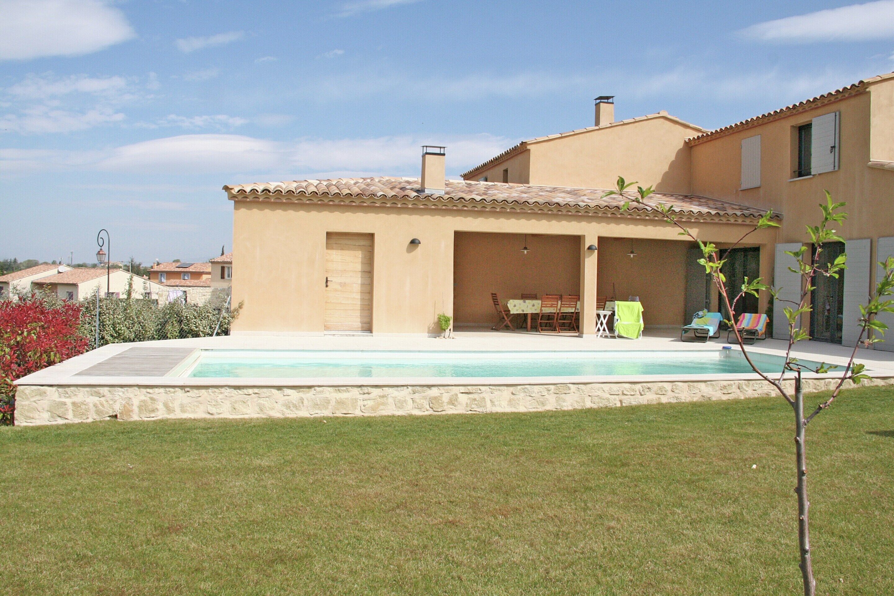 Una casa con piscina, un porche cubierto y césped.