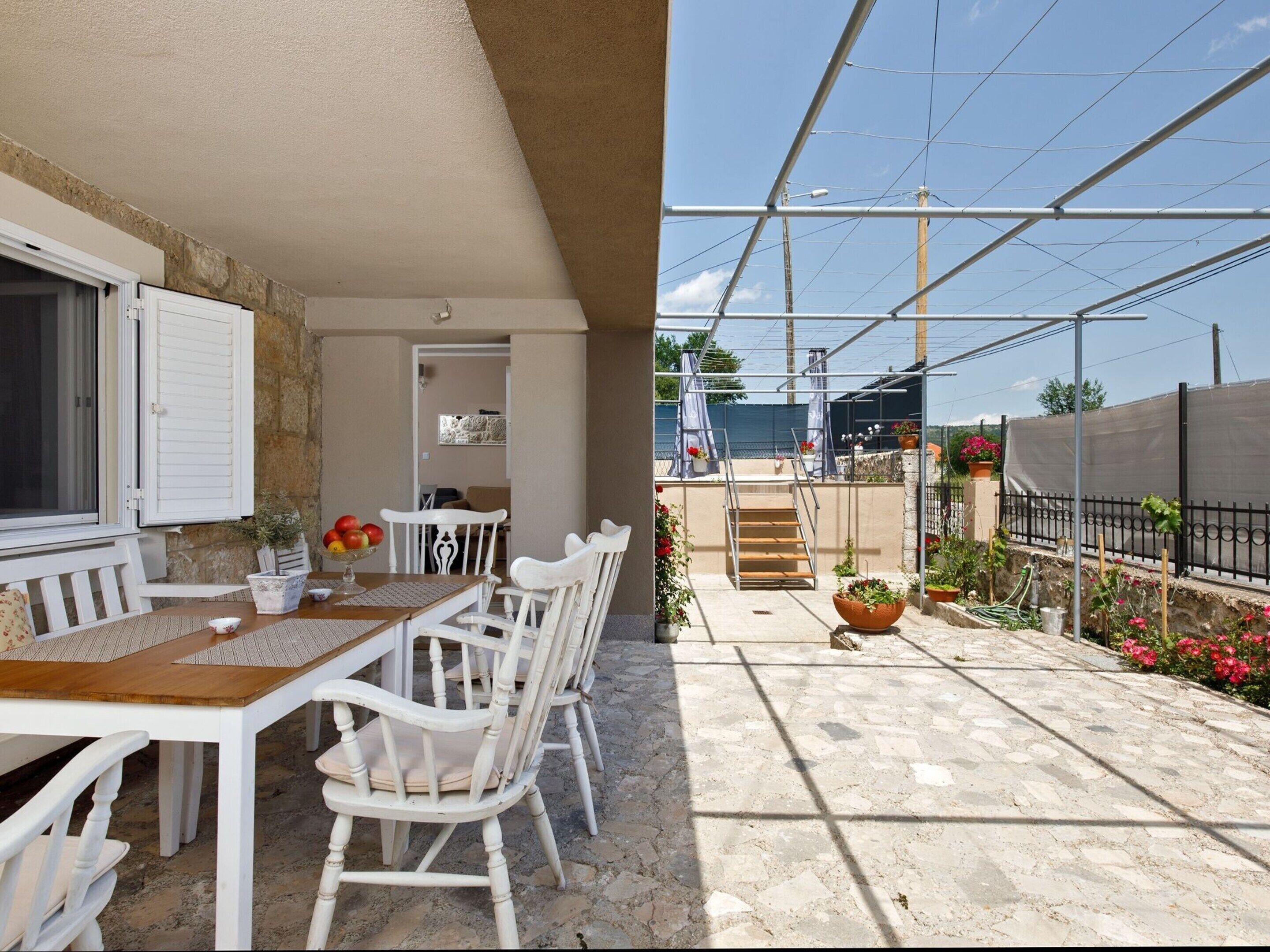 Une terrasse avec une table et des chaises, un petit jardin avec des plantes en pot et une vue sur le ciel et les lignes électriques.