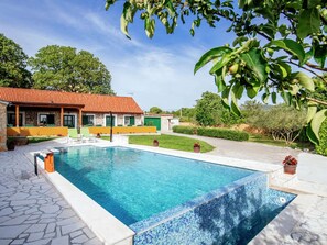 Une piscine bordée de carreaux, une maison en pierre avec un toit rouge et une pelouse bien entretenue.