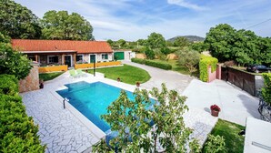 Una propiedad residencial con piscina, patio de piedra y una casa con techo de tejas rojas.