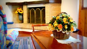 Una mesa de madera con una cesta de mimbre llena de flores, un tapete estampado y una silla.