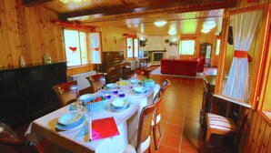 Un comedor con una mesa larga preparada para una comida, paredes de madera y una chimenea al fondo.
