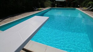Piscina rectangular con agua azul cristalina, rodeada por un solárium con baldosas y sillones blancos.