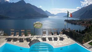Une piscine avec des chaises longues et un parasol, donnant sur un lac avec des montagnes en arrière-plan.