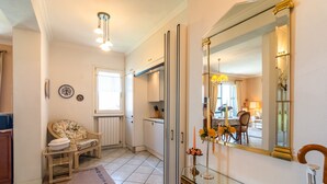 A well-lit hallway with a dining area in the background, a large mirror, and a wicker chair. - Chalet in Verbania Near Lake Maggiore (Verbania)