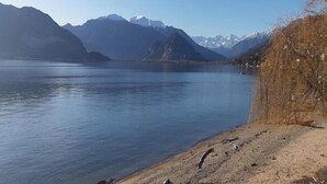 A lake with mountains in the background and a sandy shore with some vegetation. - Chalet in Verbania Near Lake Maggiore (Verbania)