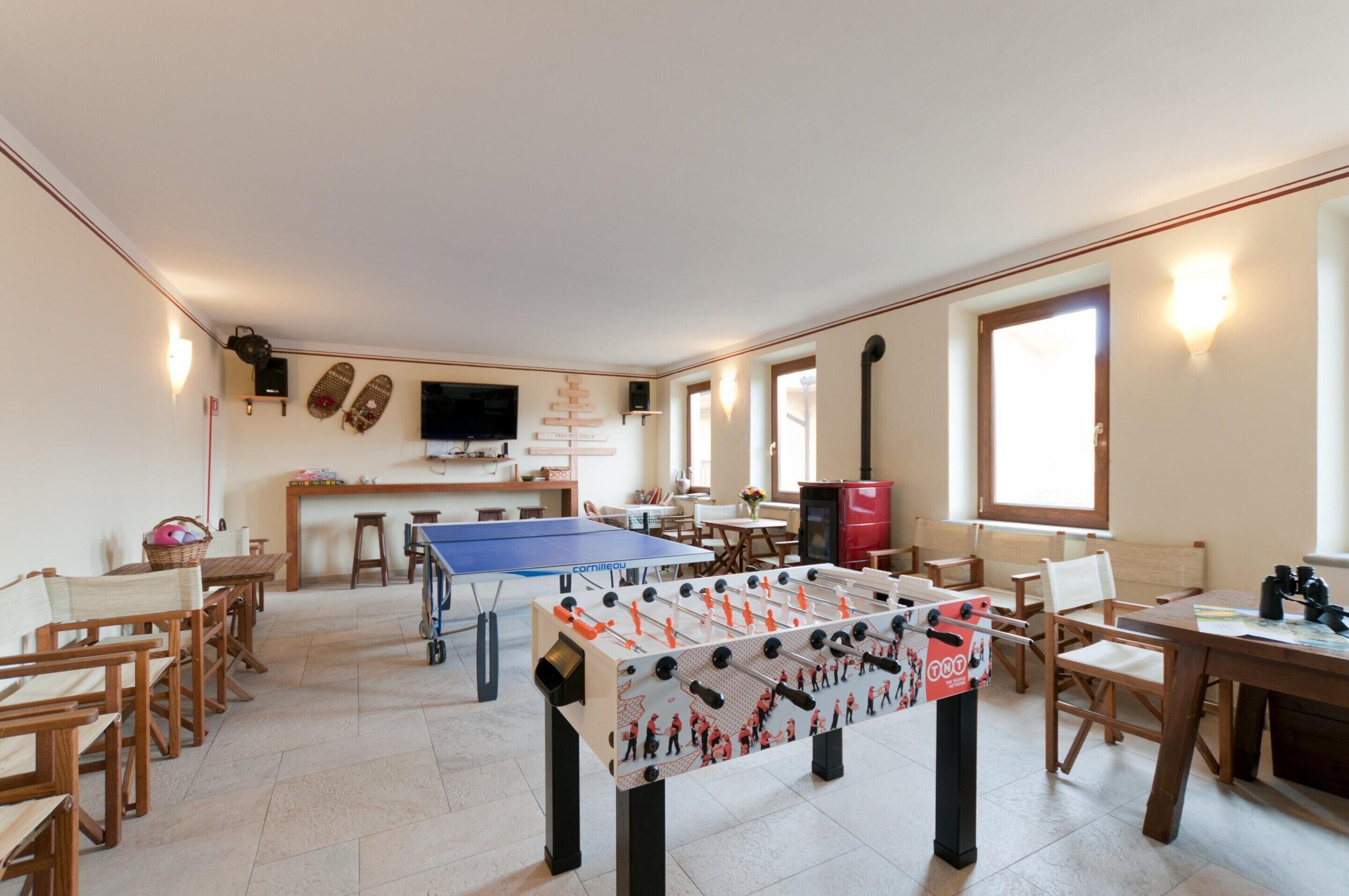 A spacious room with a foosball table, a ping pong table, and a kitchen area with a TV and bar stools.