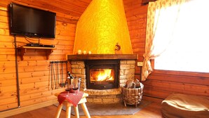 Ein gemütlicher Raum mit Kamin aus Stein, Holzwänden, einem darüber montierten Fernseher und einer bequemen Sitzecke mit Sitzsack und kleinem Tisch mit einem Weinglas.