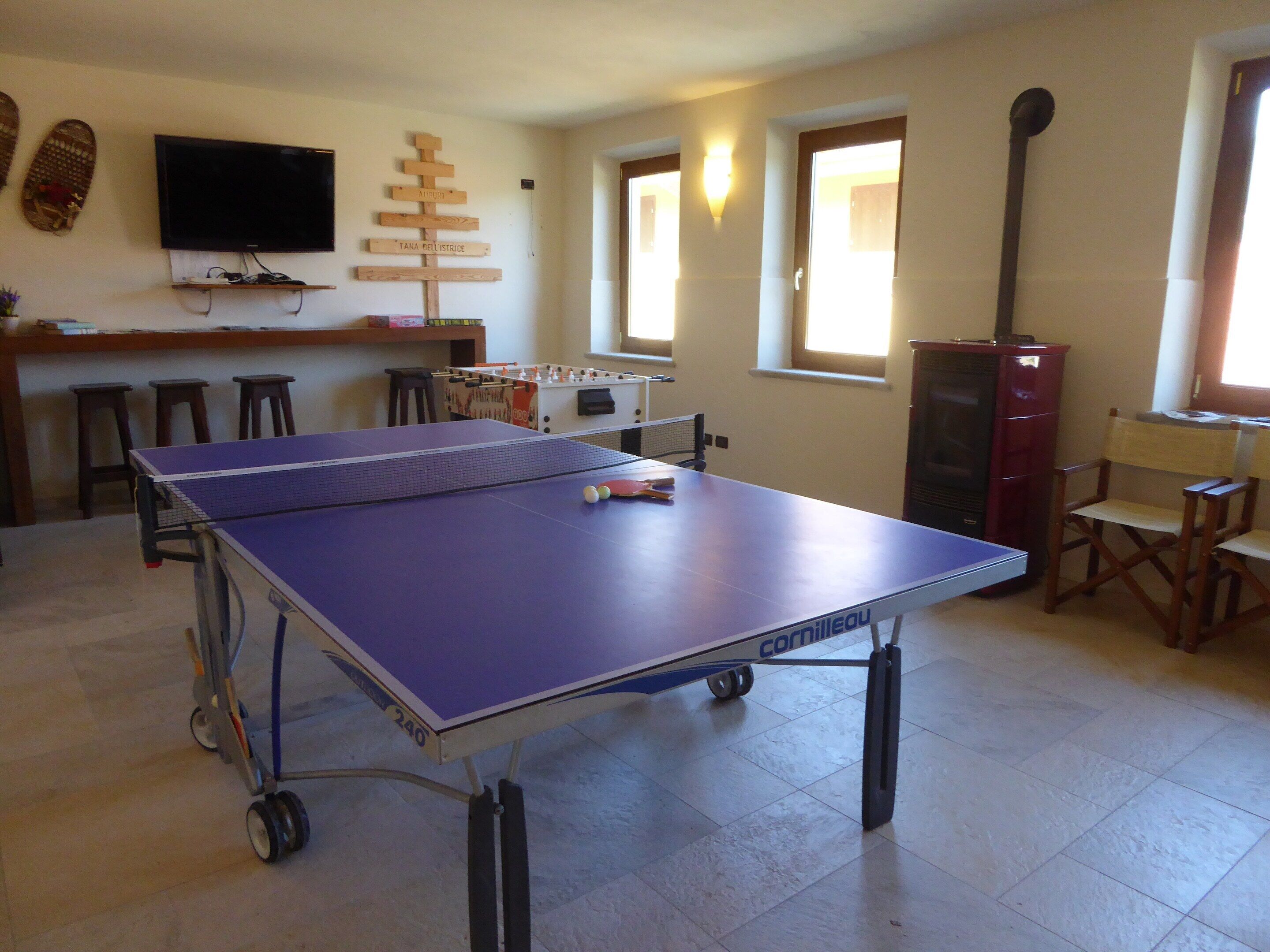 A ping pong table in a room with a foosball table, a television, and a wooden sign with names on the wall.