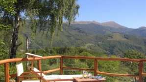 Eine Holzterrasse mit Tisch und Stühlen mit Blick auf eine gebirgige Landschaft.
